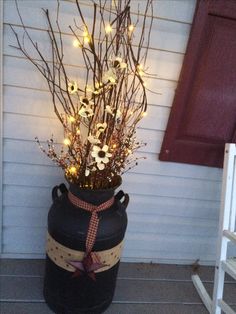 a large black vase filled with branches and lights on the side of a house next to a door