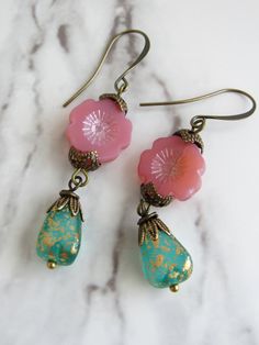 "These little dangles are made with Czech glass beads and beautiful brass filigree. The flower-shaped beads are a milky, semi-translucent pink, and the teardrops are a frosted teal with metallic gold splatters. The ear wires are antiqued brass.  The earrings are 2.5\" long from the top of the ear wires to the bottom of the dangles. Without the ear wires, the earrings are 1.75\" long. ------------------- **Please be sure to read my shipping and store policies, and don't hesitate to send me a mess Vintage Pink Flower-shaped Earrings, Handmade Vintage Pink Flower Earrings, Vintage Handmade Pink Flower Earrings, Handmade Pink Vintage Flower Earrings, Pink Handmade Vintage Flower Earrings, Handmade Pink Teardrop Flower Earrings, Bohemian Pink Earrings With Flower Charm, Elegant Pink Czech Glass Earrings, Handmade Vintage Czech Glass Flower Earrings