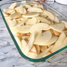 sliced apples in a glass baking dish on a marble counter top next to an egg carton