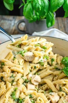 a spoonful of pasta with chicken and peas is being held over the bowl by a fork