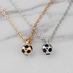 two necklaces with soccer balls on them sitting next to each other in gold, silver and rose gold