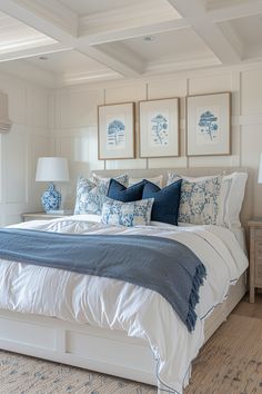 a large bed with blue and white pillows in a bedroom next to two framed pictures on the wall