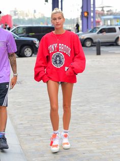 a woman walking down the street wearing a red sweatshirt and shorts with writing on it