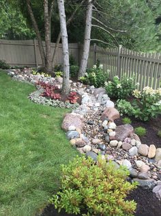 a garden with rocks and plants in the grass next to a wooden fence, surrounded by trees