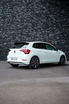 the rear end of a white car parked in front of a brick wall with black rims