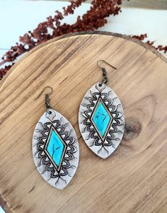 pair of earrings with turquoise stone inlays on wooden surface next to dried plant