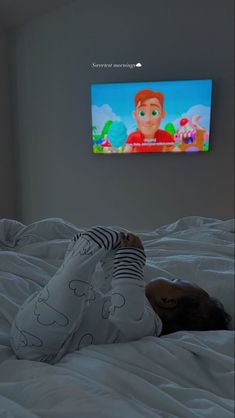 a person laying on top of a bed in front of a flat screen tv mounted to the wall