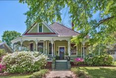 a green house with white trim and flowers in the front yard on a sunny day