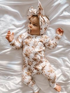 a baby laying on top of a bed wearing a white and brown floral print outfit