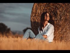 a woman sitting in the middle of a field next to a hay bale with her eyes closed