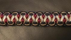 a black and red bracelet with gold accents on it's side, sitting on a brown leather surface