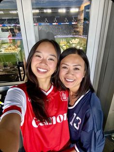 two women are taking a selfie in front of a window at a baseball game