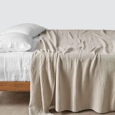 an unmade bed with two pillows on top of it and a blanket draped over the headboard