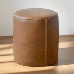 a brown leather stool sitting on top of a wooden floor