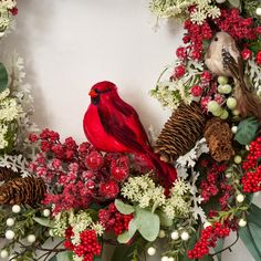 a red bird sitting on top of a wreath filled with berries and pineconis