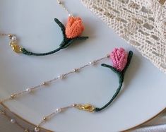 two crocheted flowers are on a plate next to pearls and beaded necklaces