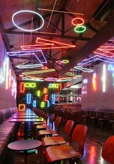 an empty restaurant with neon lights on the ceiling and tables in front of it,