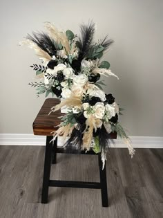 an arrangement of white flowers and feathers on a wooden table in a room with hardwood floors