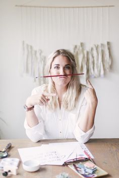 a woman sitting at a table holding a pencil in front of her face and looking up