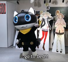 a cat mascot standing in front of some anime character cut outs on the wall behind it