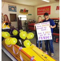 a man and woman holding a sign in a garage with balloons on the floor next to them