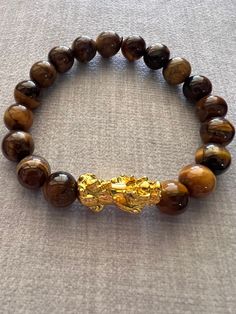 Item Details: Natural Tiger's Eye Gemstone Beads 12mm w/ lucky Feng Shui 24K Gold Plated Pixiu or Pi Yao Bracelet. Suitable to wear for every day to match any outfits. Good for gifting to your family and friends. Gemstone: Tiger's Eye is a root and sacral chakra stone which means it helps you to get grounded, build a safe and strong foundation, and find your motivation once more. It's also good at warding off negative energy. It gives one the courage to step out of their comfort zone and take action to achieve their goals. It amplifies the energies of other crystals as well as one's intentions. It can help one feel confident and self-empowered, and reduce the need for approval from other people. Tigers Eye is good for growing your confidence and strength and it is known as the stone of cou Handmade Gold Stretch Bracelet For Meditation, Gold Spiritual Stretch Bracelet With Gemstone Beads, Gold Bracelets With Polished Beads For Healing, Gold Bracelets With Round Beads For Good Luck, Gold Beaded Good Luck Bracelets, Gold Stretch Bracelet With 8mm Beads For Meditation, Gold Stretch Bracelet With Natural Stones For Meditation, Gold Stretch Bracelet With Natural Stones, Gold Crystal Bracelet With 8mm Beads As A Gift