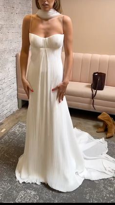 a woman in a white dress standing next to a couch with her hands on her hips