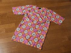 a pink and orange flowered shirt laying on top of a wooden floor next to a pair of scissors