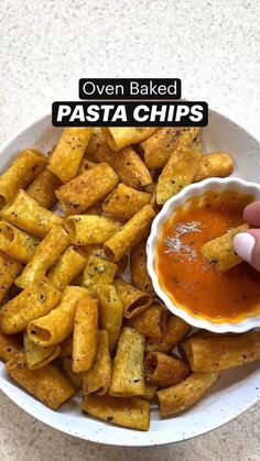 a person dipping sauce on top of pasta chips in a white bowl with text overlay that reads oven baked pasta chips