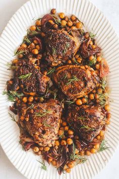 a white plate topped with meat covered in chickpeas and garbanzo beans