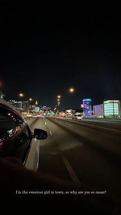 a car driving down the road at night with city lights in the backgroud