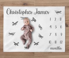 a baby laying on top of a wooden floor next to a wall calendar with an airplane design