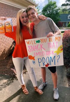 two girls holding up a sign that says will you be my snack that smiles back at prom?