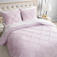 a bed with pink comforter and pillows in a white room next to a night stand