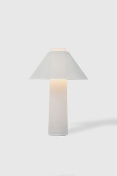 a table lamp with a white shade on the top and bottom, in front of a gray background