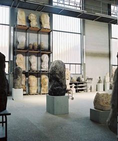 several sculptures are displayed in a room with glass walls and shelves full of stone heads