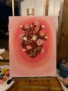 a painting with flowers in the shape of a heart on a easel next to paintbrushes