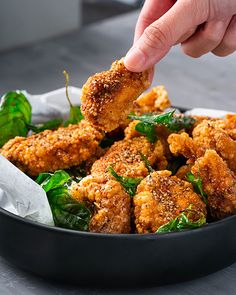 a person dipping something into a bowl filled with greens and fried chicken pieces in it