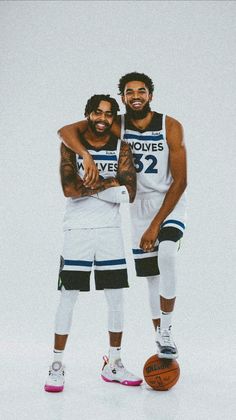 two men standing next to each other in front of a white wall holding basketballs