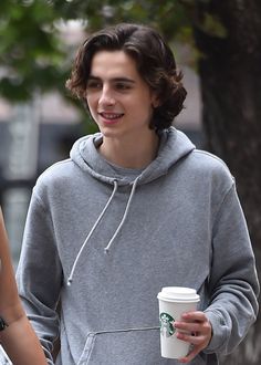 a young man is holding a coffee cup and talking to another person on the street