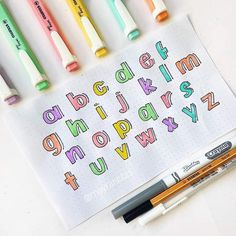 some markers and pens are laying on top of a sheet of paper that has the letters written in different colors