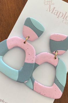 two pink and blue earrings sitting on top of a table next to a white card