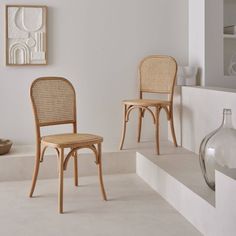 two wooden chairs sitting next to each other in a room with white walls and flooring