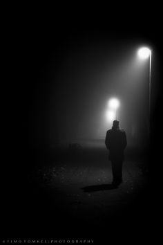 a person standing under a street light on a foggy night in black and white