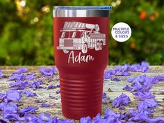 a red tumbler with the name adam on it and purple flowers in the background