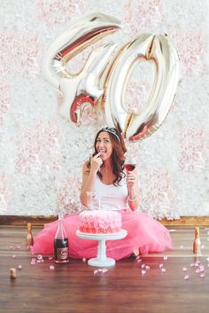 a woman sitting on the floor in front of a cake with balloons and confetti