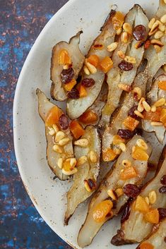 a white plate topped with sliced up pears and nuts on top of a blue table