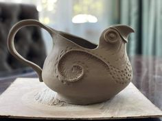 a ceramic bird shaped vase sitting on top of a wooden table next to a window