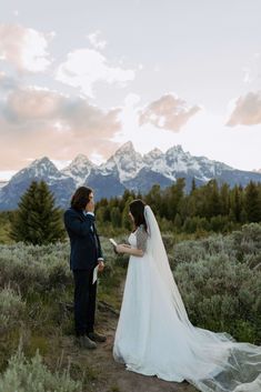 a bride and groom standing in front of the mountains