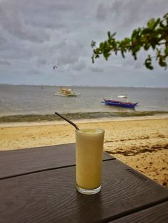 a drink sitting on top of a wooden table next to the ocean